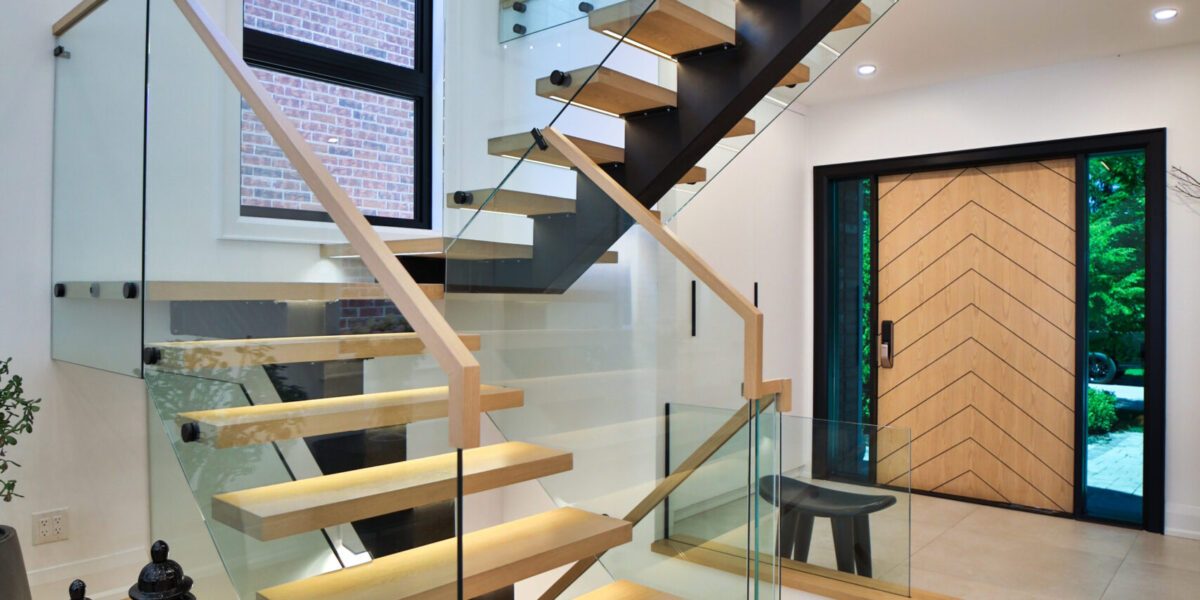 A renovated modern open concept home foyer featuring a large custom wooden front door and staircase.