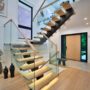 A renovated modern open concept home foyer featuring a large custom wooden front door and staircase.