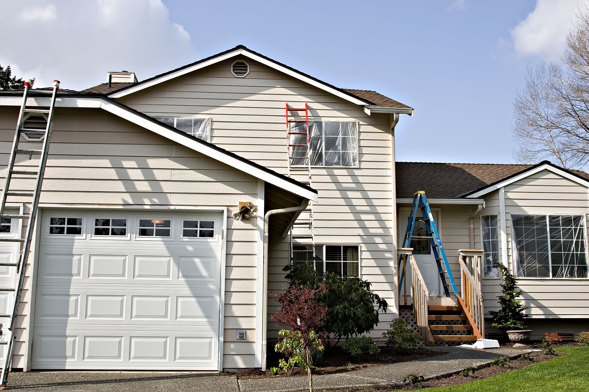Two-storey house with ladders for exterior painting on sunny day