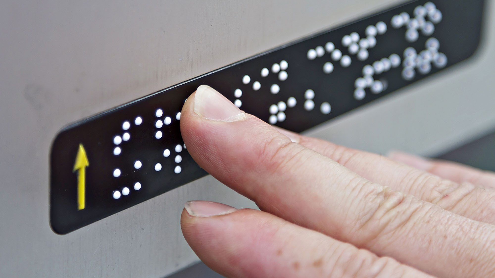 Close-up of hand reading Braille on an elevator button panel