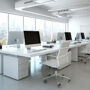 Modern open-plan office interior with sleek white desks and large windows