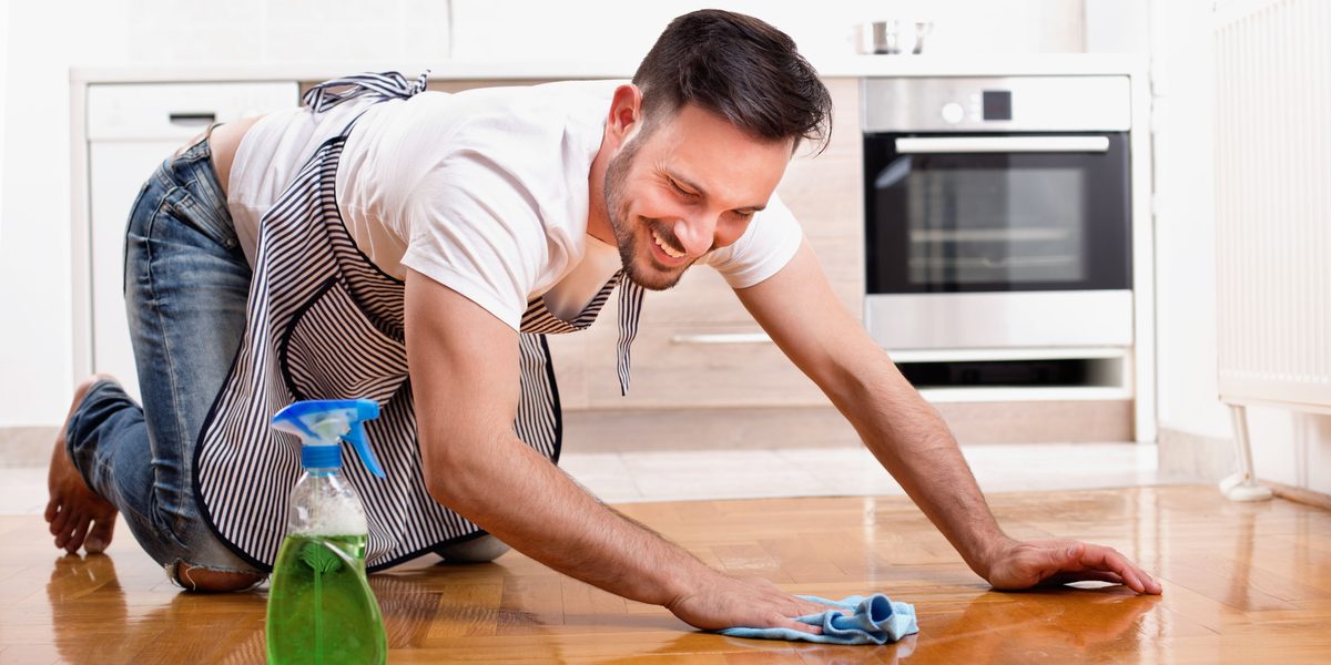 Man smiling while cleaning wooden floor with spray and cloth