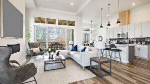 open concept living room with stylish furniture electric fireplace grey leather arm chairs windows revealing blue sky hardwood floors and view to kitchen