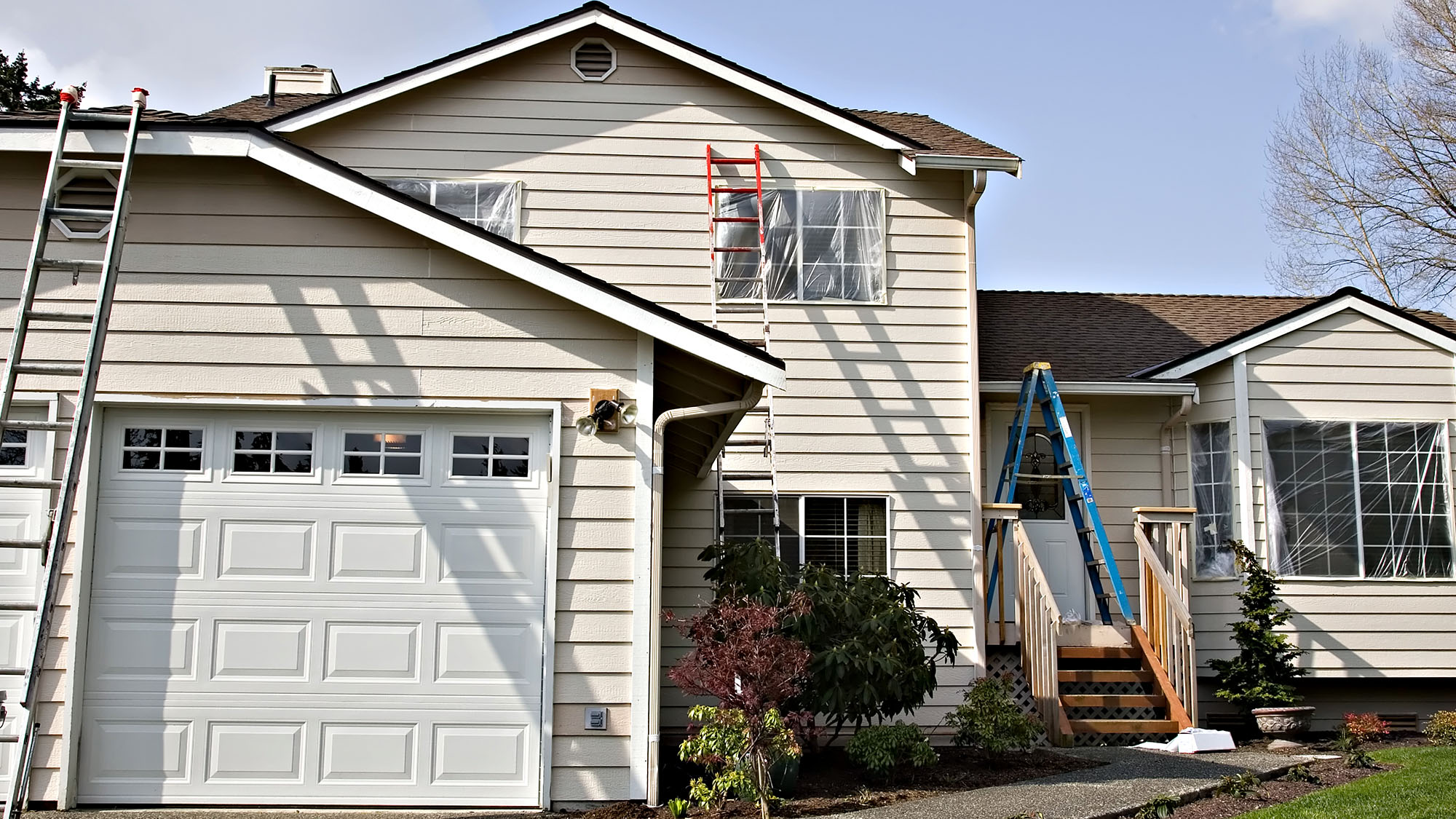 House exterior prepared for painting with ladders and plastic coverings