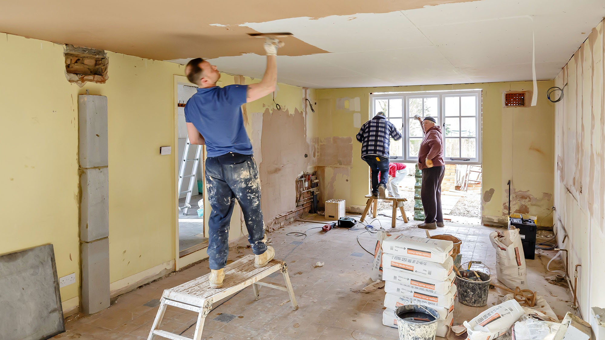 Home renovation with workers plastering ceiling and preparing walls