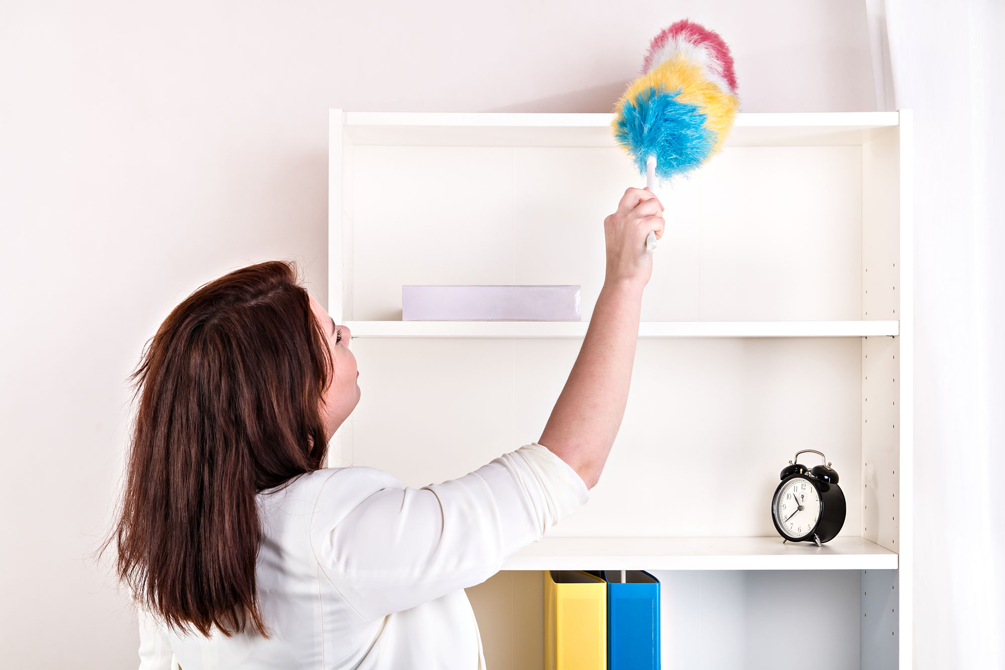 Woman dusting shelf with a colourful duster in a home setting