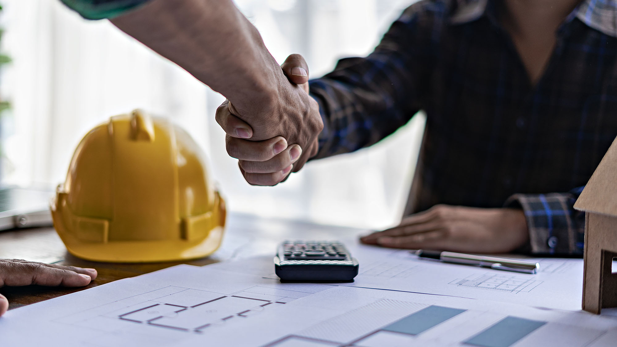 Business handshake over construction plans and safety helmet