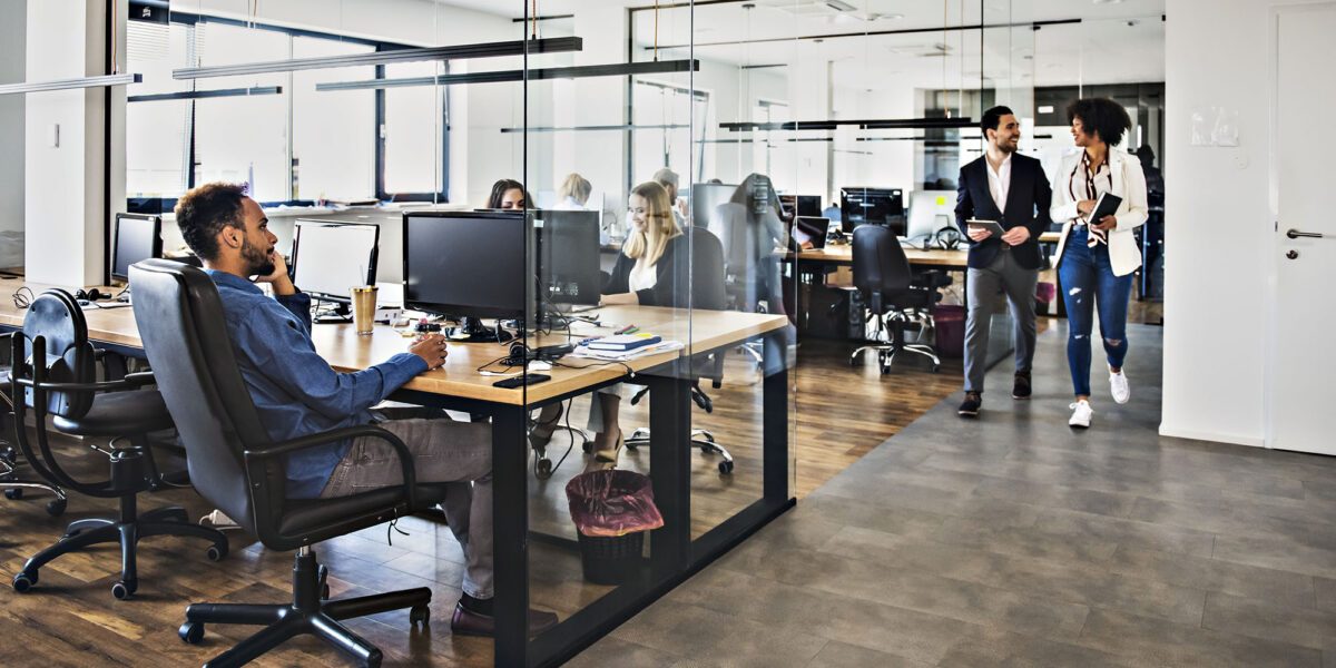Dark wooden floor and an open space office, a lot of employees working in the office, women wearing business clothes, men wearing elegant shirts and trousers, brainstorming, organising the working process, working on some new projects, glass walls in the office.