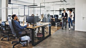 Dark wooden floor and an open space office, a lot of employees working in the office, women wearing business clothes, men wearing elegant shirts and trousers, brainstorming, organising the working process, working on some new projects, glass walls in the office.