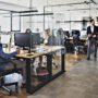 Dark wooden floor and an open space office, a lot of employees working in the office, women wearing business clothes, men wearing elegant shirts and trousers, brainstorming, organising the working process, working on some new projects, glass walls in the office.