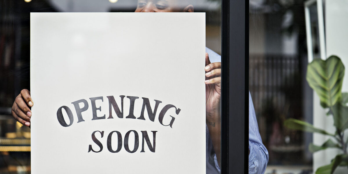 Storefront with 'Opening Soon' sign held by a person