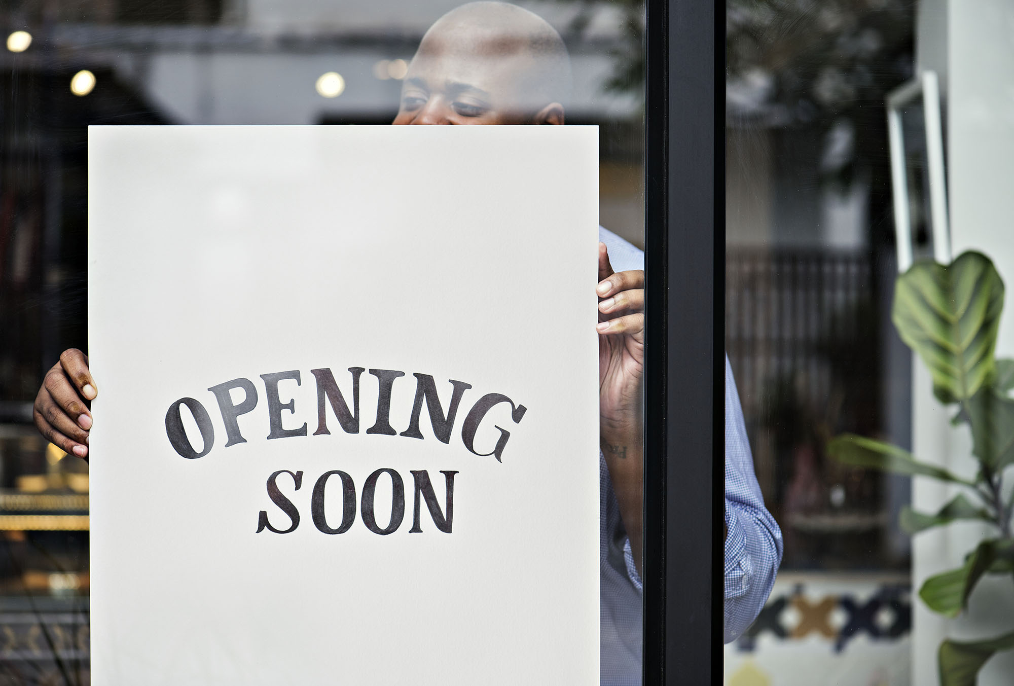 Storefront with 'Opening Soon' sign held by a person