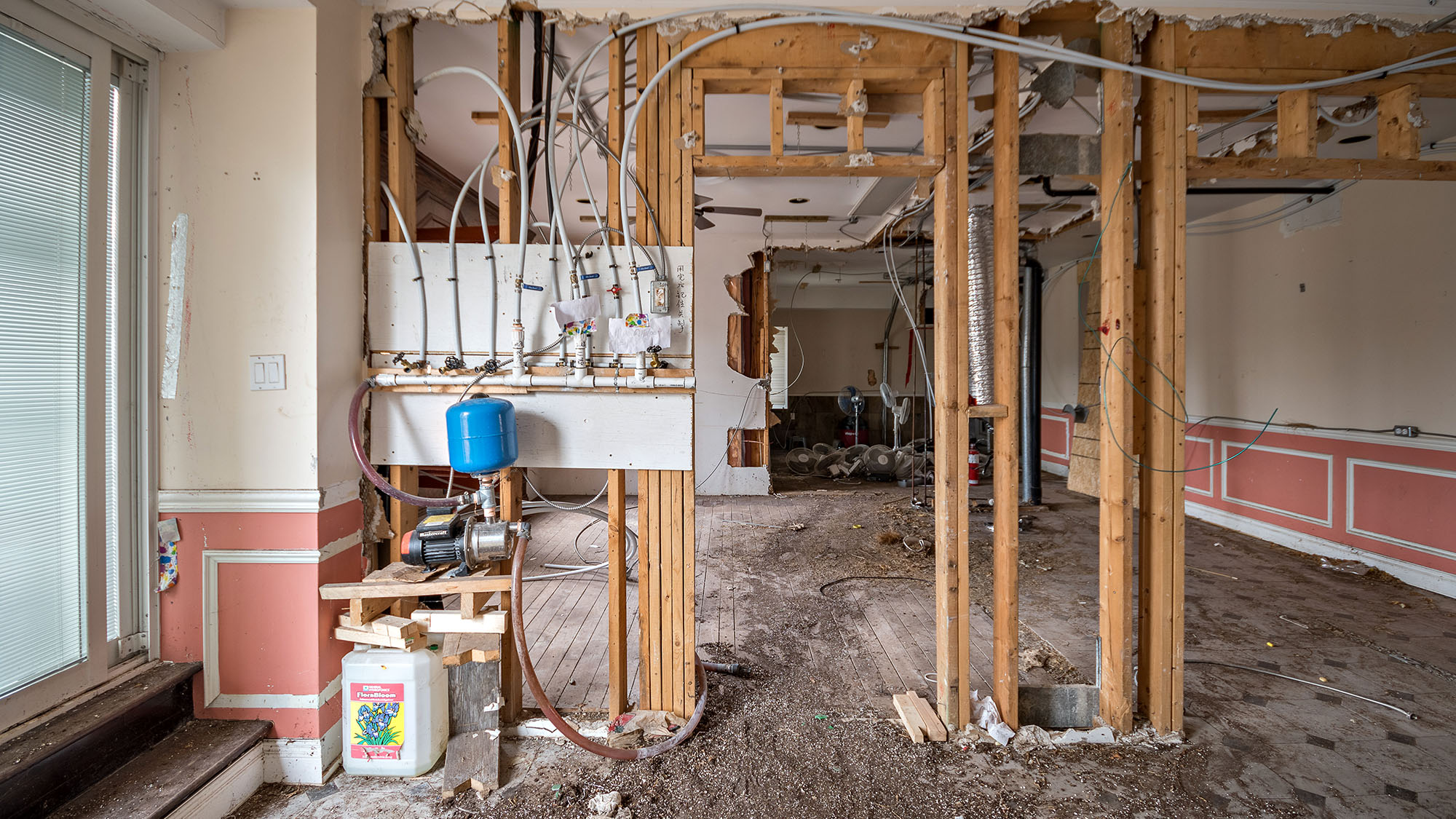Interior renovation showing exposed pipes and wiring in a gutted room