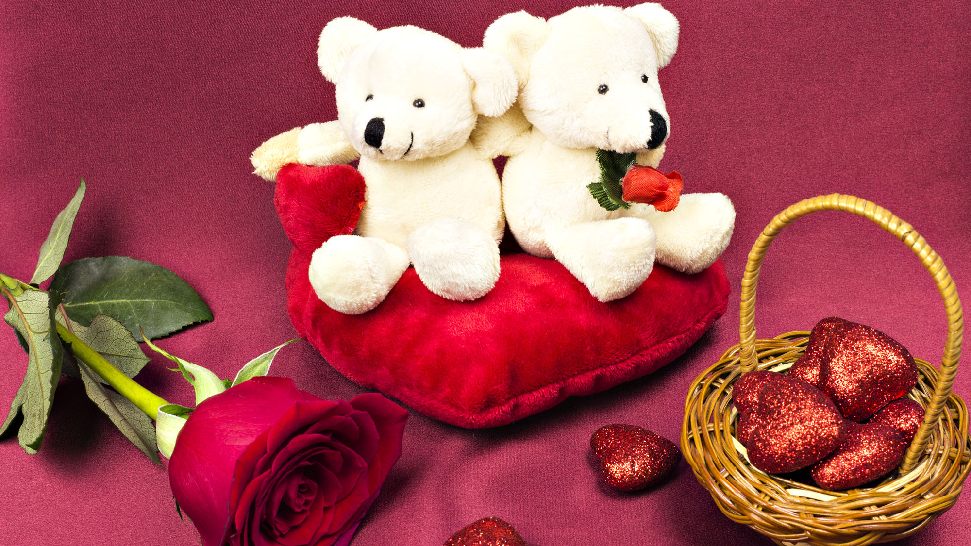 Two teddy bears on red cushion with roses and heart-shaped chocolates