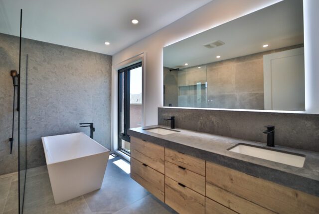 A renovated bathroom with tub, floating vanity, double sinks and edge lit mirror.